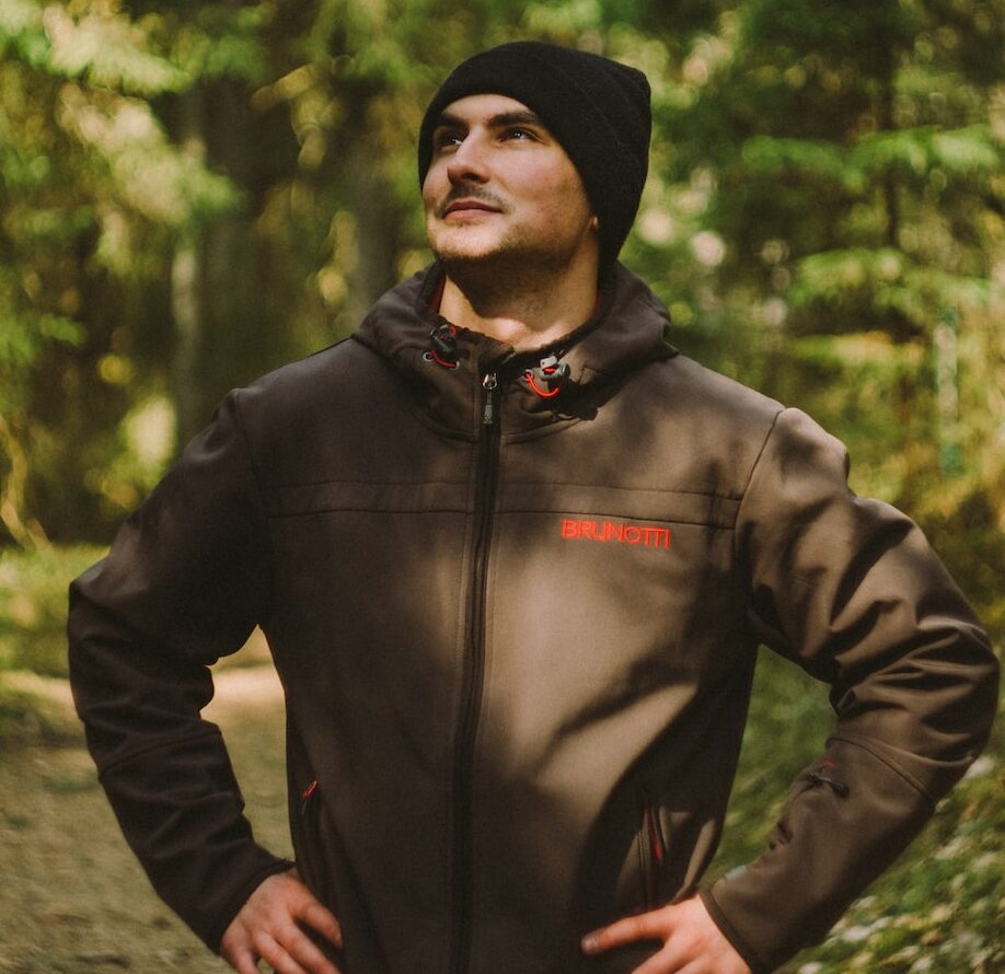 uomo con giacca nera con zip in piedi nella foresta durante il giorno